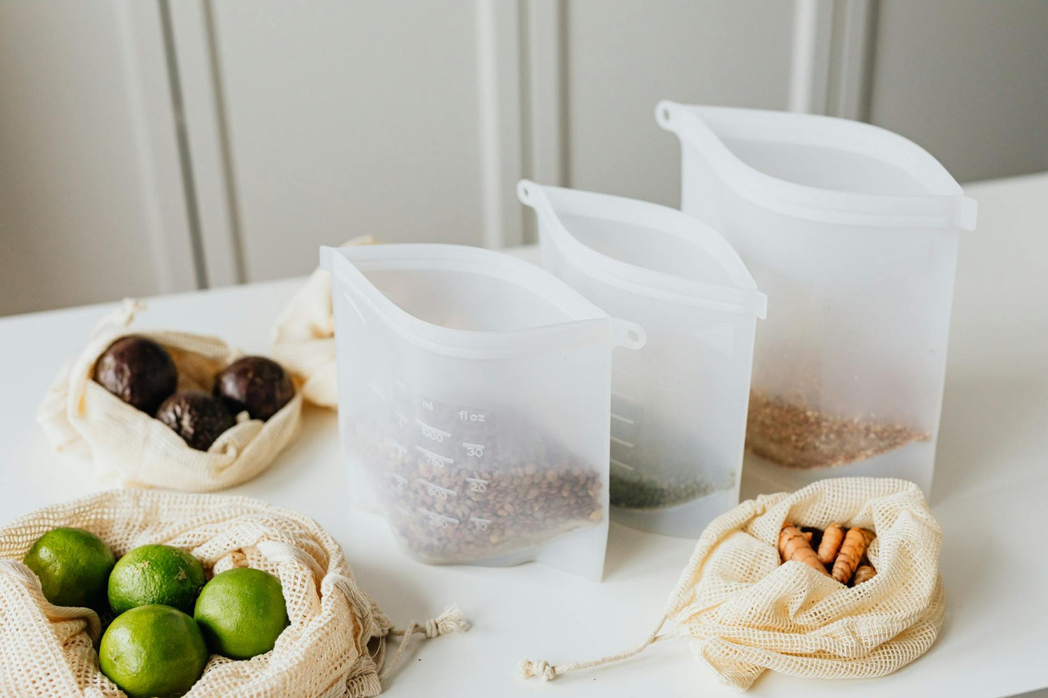 Silicone bags and reusable mesh bags with groceries on a white surface.