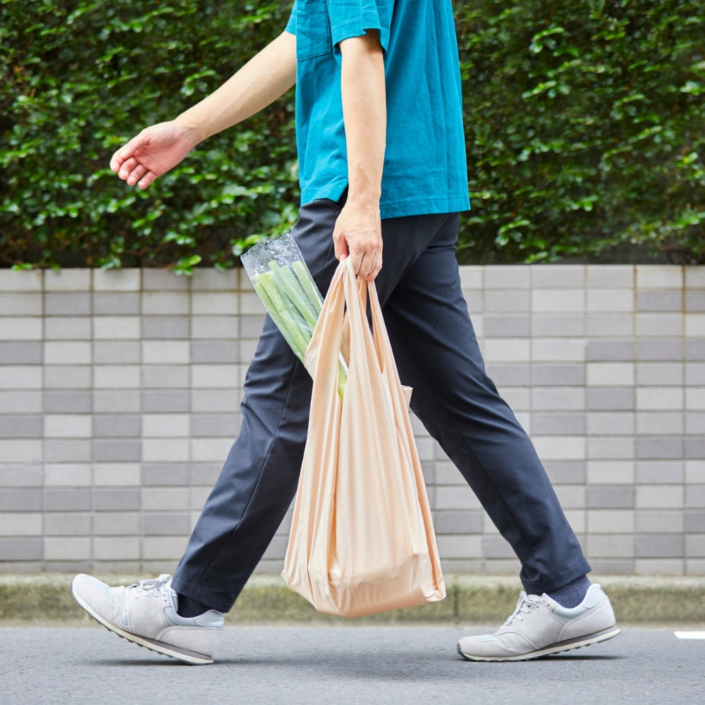 Person walking outdoors holding a reusable bag and a package